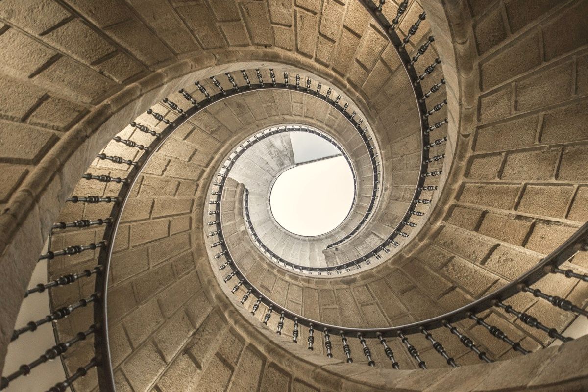 Escalera de caracol de piedra vista desde abajo, girando hacia la luz de una claraboya.