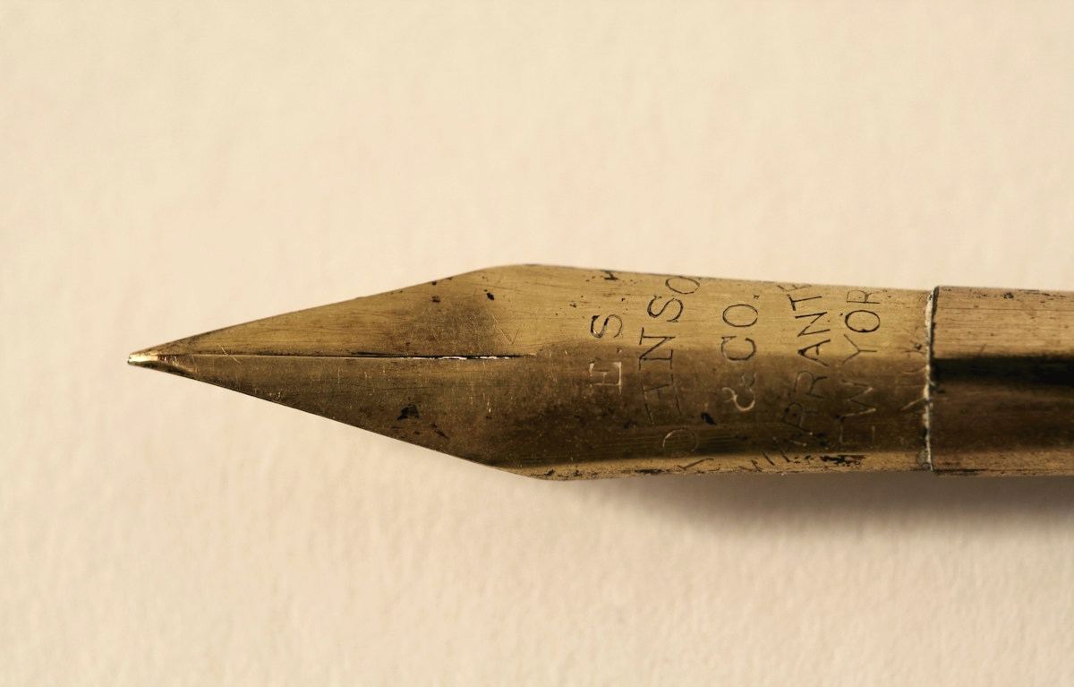 Plumilla dorada de una pluma estilográfica sobre papel claro.